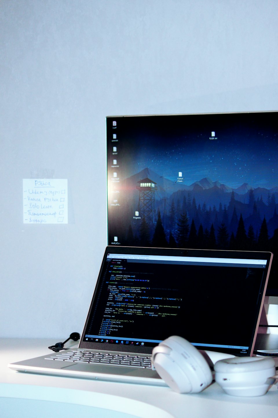 A laptop showing code sits on a desk with headphones.